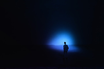 A picture of a miniature man stands in the spotlight looking forward.Concept of facing the unknown, taking a decision and finding solution.