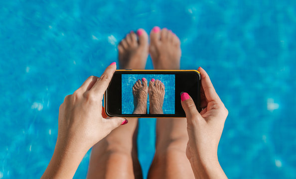 Woman taking pictures of her feet nails in the pool