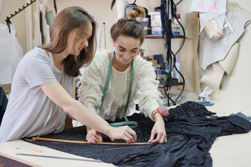Seamstresses measure the fabric for sewing a dress in the atelier. Two female tailor working in in...