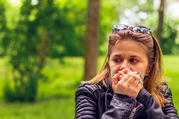 Fototapeta premium Young woman with brown hair wearing sunglasses covering her mouth with both hands in nature – Portrait of a pretty girl with expressive facial features