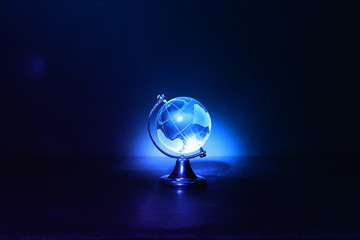 Small crystal globe in front of dark and dramatic light.global issues concept