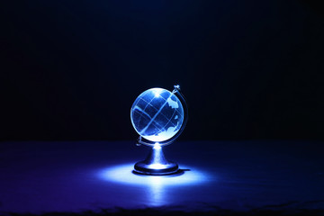 Small crystal globe in front of dark and dramatic light.global issues concept