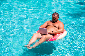 Male businessman with a laptop on rubber ring in the water
