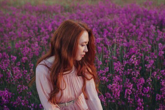 Profile portrait of charming redhead woman posing among violet flowers