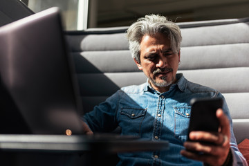 Handsome man using phone and laptop in a modern office.