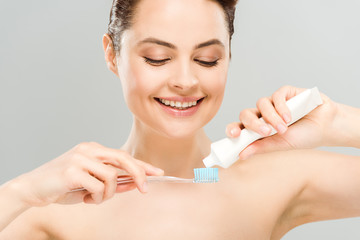cheerful naked woman holding toothpaste near toothbrush isolated on grey
