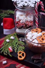 Hot chocolate with marshmallows and pretzels in a cup and a dry mix for preparing the drink in a glass jar