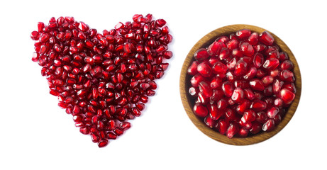 Heart shape pomegranate seeds on white background. Pomegranate seeds in a wooden bowl isolated on white background. Background made of red pomegranate seeds. The scattered red grains of granate.