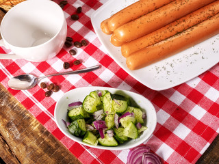 Sausage portion with bread baguette on table setting on checkered tablecloth and cup in farm style. Delightful, unique taste.