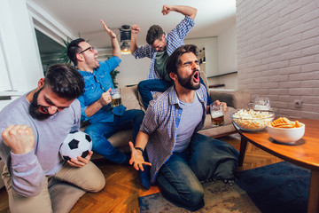 Men watching sport on tv together at home screaming cheerful. Group of friends sitting on the couch and watching a football game.