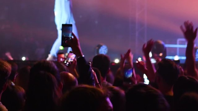 people at the concert who dance and sing with their arms in the air and resume with their mobile phone all in a purple light