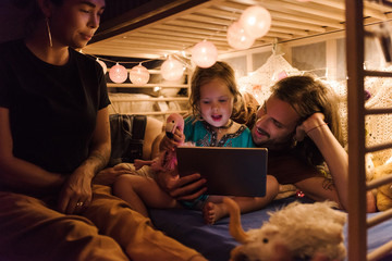 Family with tablet on small bed in lights
