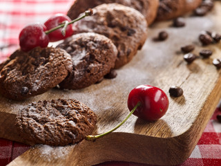 Oatmeal chocolate cookies with coffee grains and cherry, powdered sugar on kitchen cutting board with checkered fabric on wooden table in village style for picnic. Eat dish can be both hot and cold.