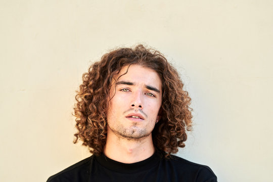 Handsome man with curly hair on pale background.