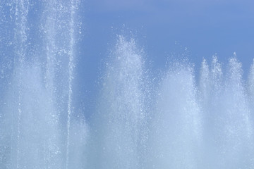 Splashing water from a fountain close up against the blue sky.