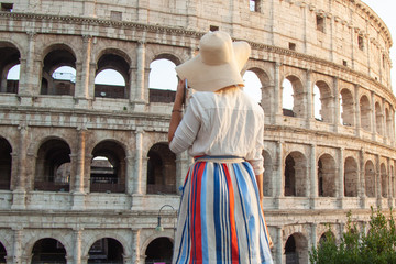Fototapeta na wymiar Beautiful young woman in fashion dress alone standing in front of colosseum in Rome at sunset.