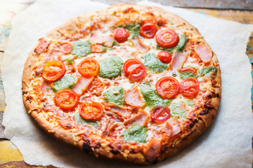 Pizza with prosciutto, ham, green pesto and tomatoes 