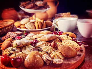 Oatmeal cookies and sand chocolate cake with cherry on cutting board on wooden table in rustic style served with cups and dessert spoons. Several recipes for baking.