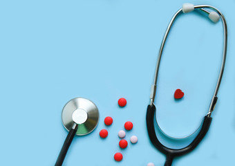 stethoscope on a blue background with pills and a red heart, free space, concept medicine, heart disease, treatment.,and a doctor's office.