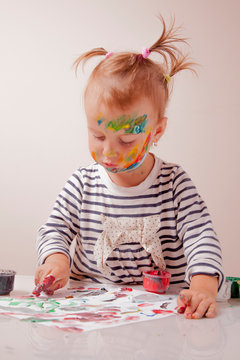 Cute little child girl painting with colorful hands and finger.