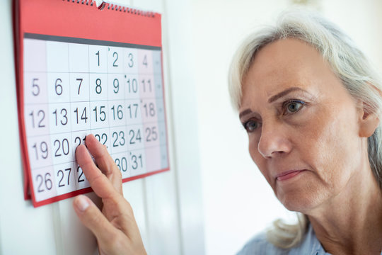 Confused Senior Woman With Dementia Looking At Wall Calendar