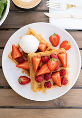 Delicious breakfast in the summer cafe. On a wooden table, a dessert of Viennese waffles with a scoop of ice cream and fruit berries of strawberry and raspberry. View from above. Top view.