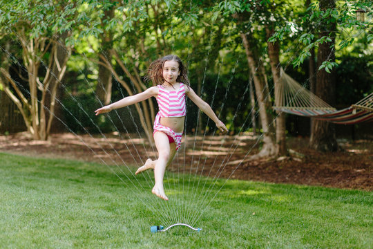 Young girl jumping through a water sprinkler