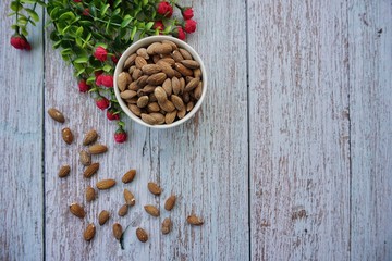 Almonds nuts in bowl with a small pink flower on blue wood background, top view