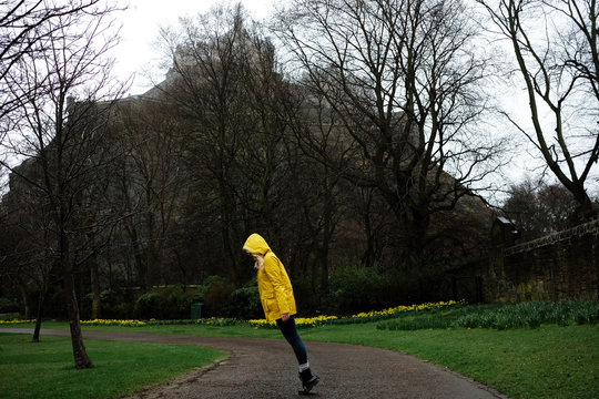 woman wearing a yellow raincoat in the middle of a path at a park