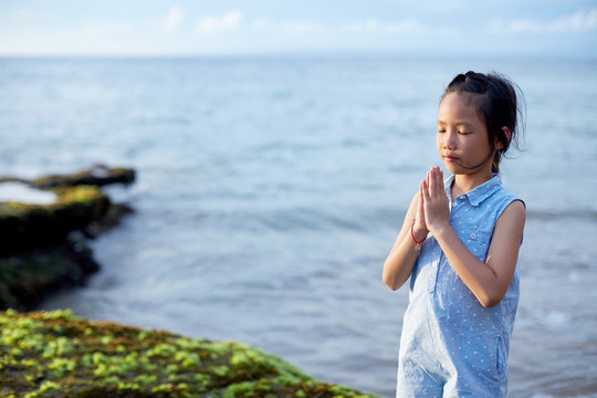 Cute beautiful asian little girl praying with hands closed at the seaside