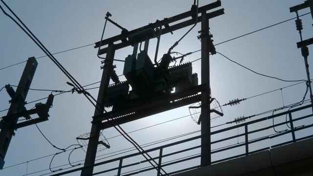 City electric transformer above the ground on two pillars against a blue sky and sun on the street Delhi, India. Shot in motion