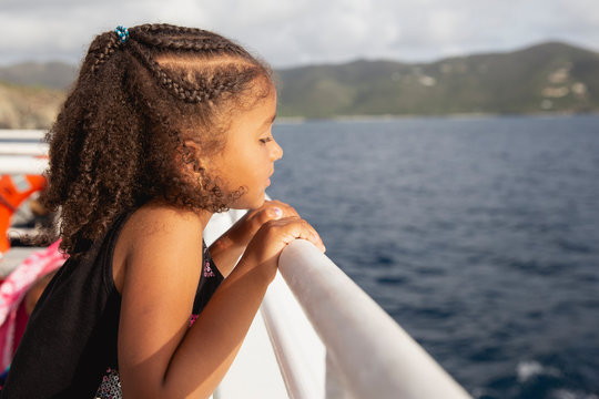 Child with curly hair looking over the side of a ferry boat at the water