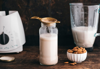 Food: Almond milk in a bottle with some almonds besides and blen