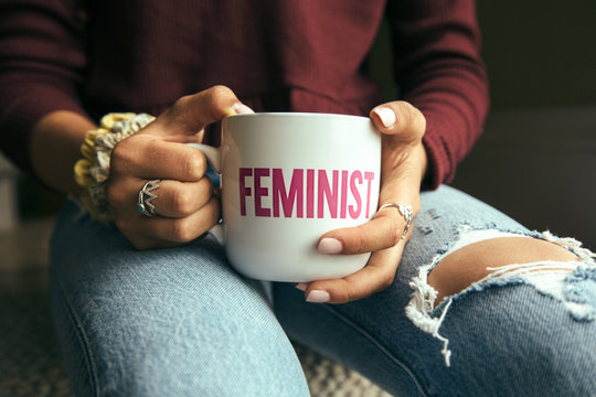 Female holding a mug with the word Feminist on it.