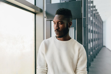 Young black man with pensive expression looking out window