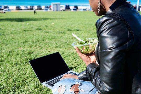Unrecognizable lady working and having lunch with laptop in park.