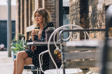 Attractive young Australian woman drinks coffee at cafe in sunshine
