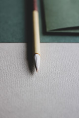 Close up of green coloured fine art paper, a green envelope with a golden seal and a wooden calligraphy brush laying on top of it