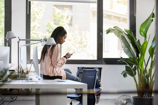 Businesswoman Using Phone While Sitting On Desk