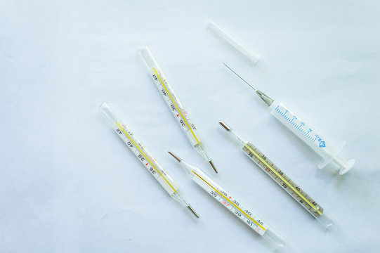 Four mercury thermometers and a disposable medical syringe on a white background