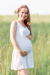 Fototapeta na wymiar Beautiful pregnant woman in white dress in the meadow