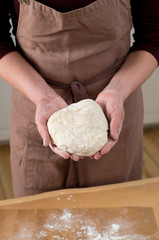 Female hands holding raw dough and wooden table