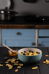 Bowl with delicious cornflakes with berry and honey on black table in the kitchen. Healthy food.
