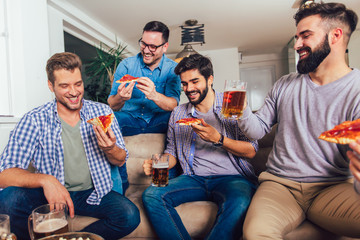 Group of four male friends drinking beer and eating pizza at home.