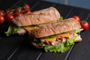 Baguette with ham, cheese, tomatoes, lettuce and cucumber on black table. Fresh breakfast. Delicious food. Kitchen. Snack.