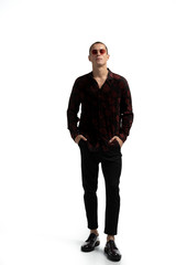 Full length portrait of amazing attractive man in stylish trendy clothes, wearing red sunglasses, holding hands in pockets, looking at camera.