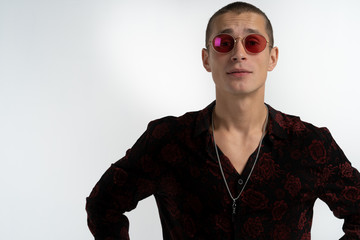 Happy young attractive man with short haircut in red sunglasse, wearing trendy black shirt, looking at the camera, isolated over white background