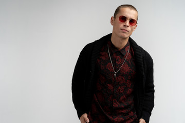 Serious confident attractive young man with short haircut in red sunglasses wearing stylish black sweater and shirt, looking at the camera