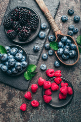 Obraz na płótnie Canvas Fresh berries with raspberries, blueberries, blackberries in bowl on a stone stand on a dark metal background.