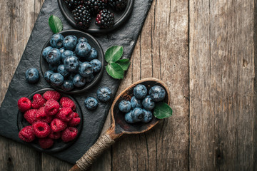 Obraz na płótnie Canvas Fresh berries with raspberries, blueberries, blackberries in bowl on a stone stand on wood background.